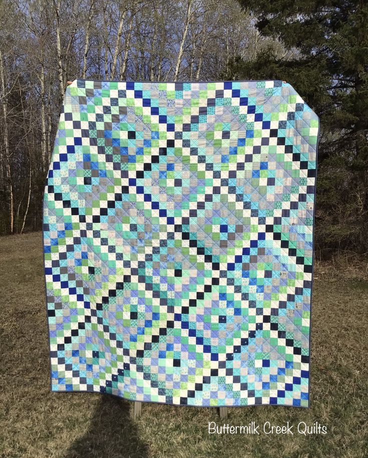 a blue and green quilt is hanging on a clothesline in the grass near some trees