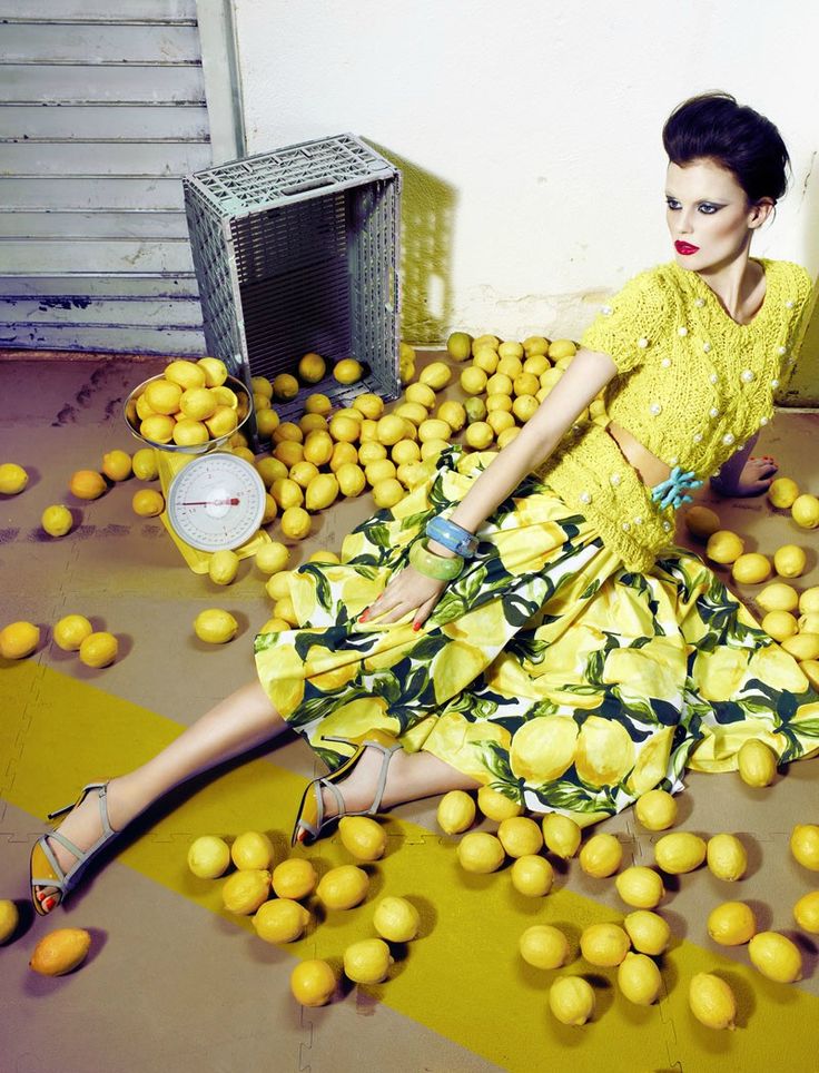 a woman in a yellow dress sitting on the ground surrounded by lemons and a clock