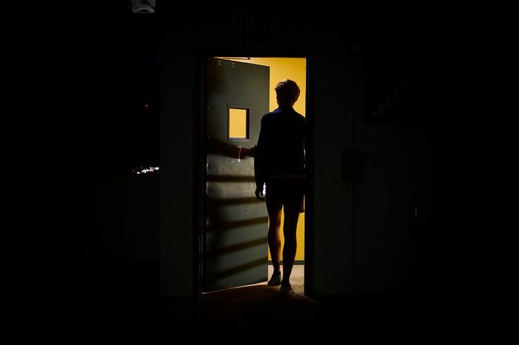 a person standing in an open doorway at night with their hand on the door handle