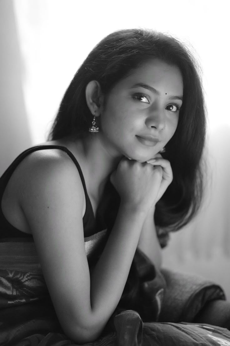 a black and white photo of a woman sitting on a bed with her hand under her chin