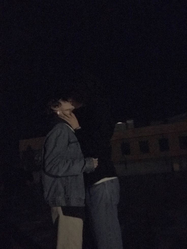 two people standing next to each other in the dark at night with one person covering his face