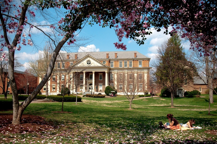 two people are sitting on the grass in front of a large brick building with columns