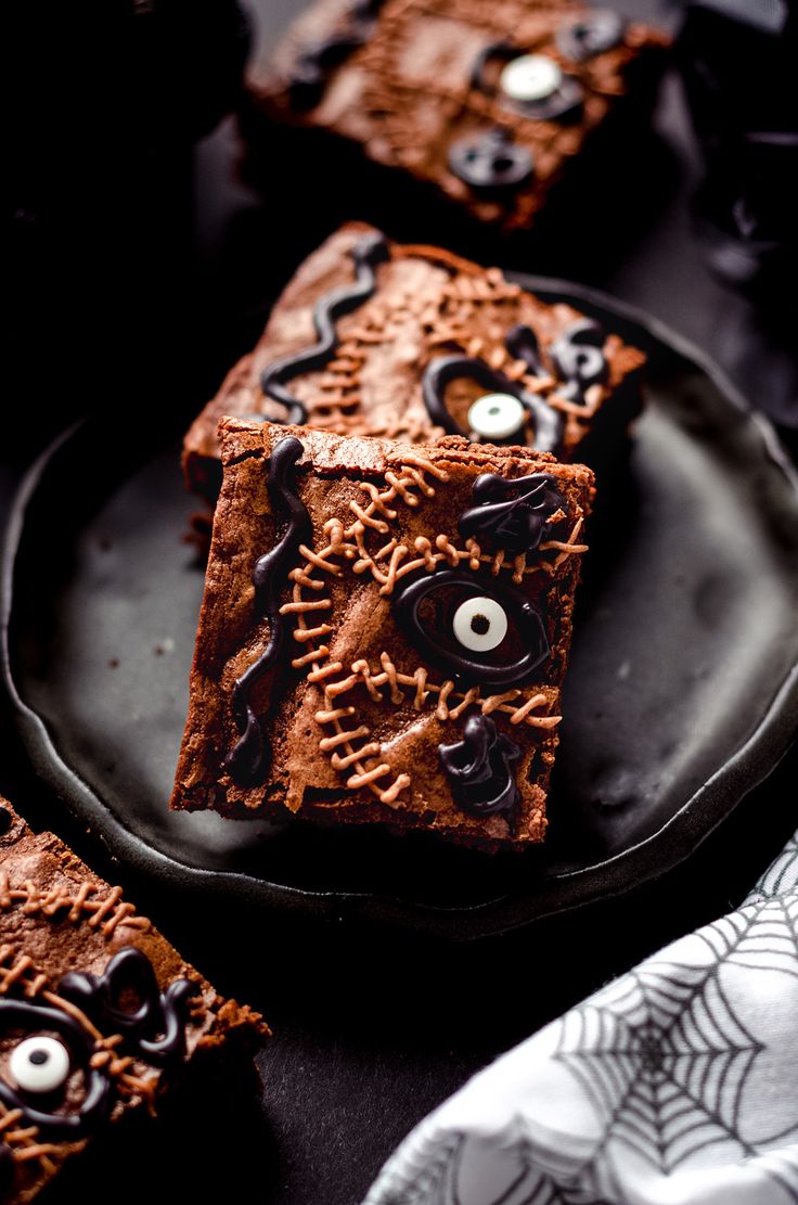 halloween brownies decorated with googly eyes and spider webs on a black plate