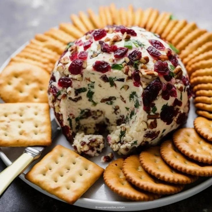 a cheese ball with cranberries and crackers on a plate next to some crackers