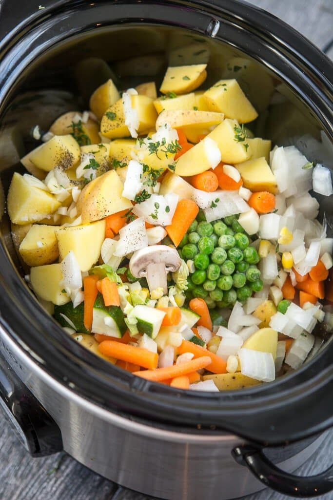 a crock pot filled with potatoes, peas and carrots on top of a wooden table