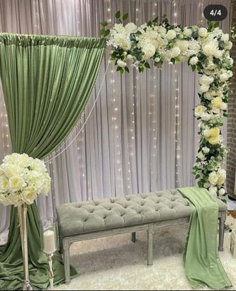 a green and white wedding set up with flowers on the back of a bench next to a window