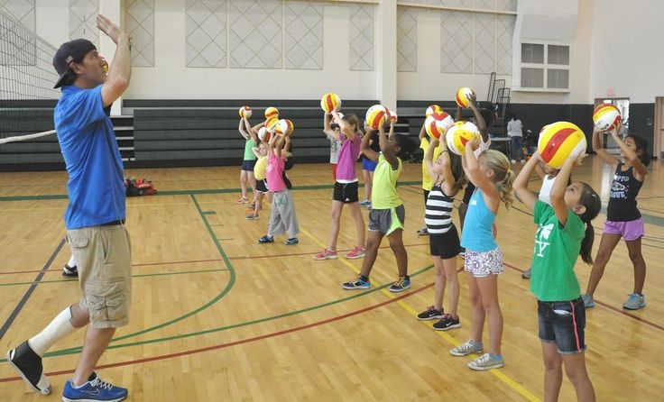 a group of young children holding up beach balls on top of a wooden floor in a gym