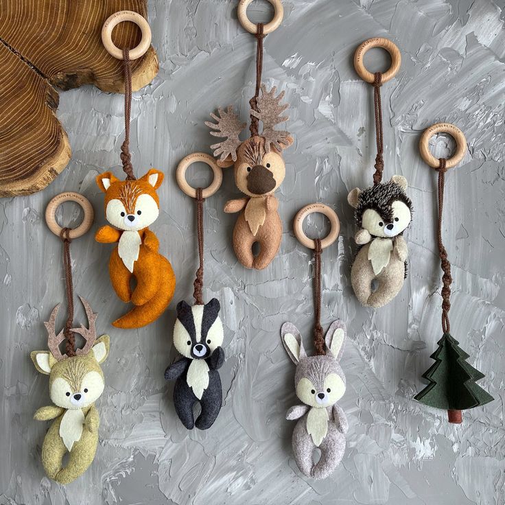 several stuffed animals hanging from hooks on a gray wall with leaves and branches in the background