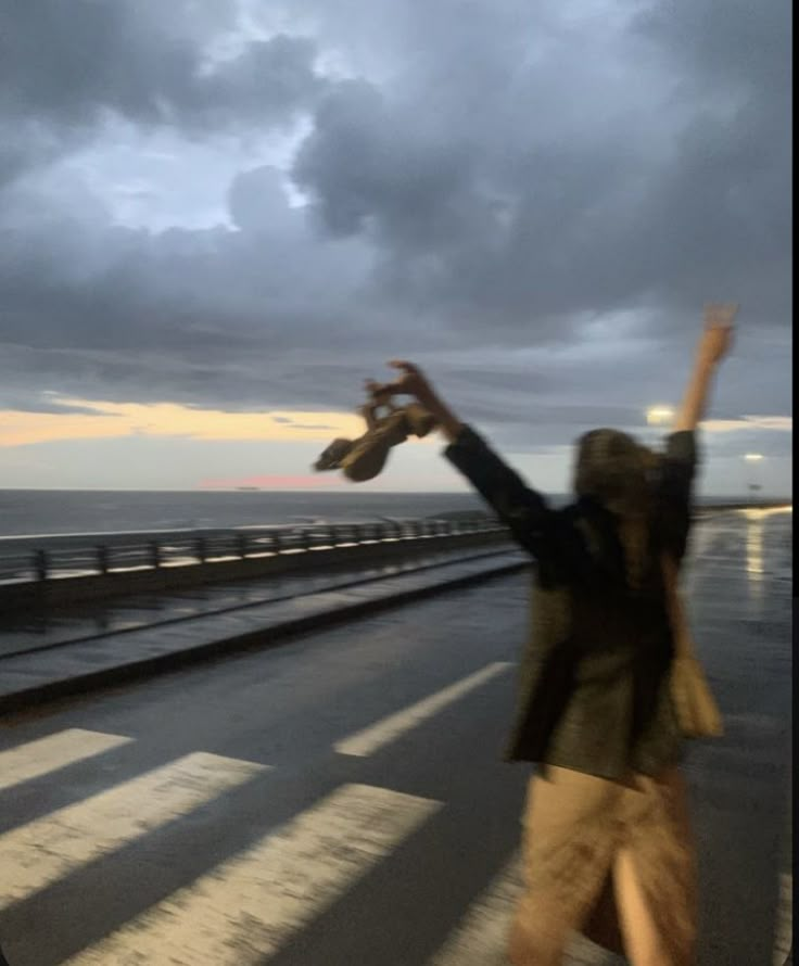 a woman standing on the side of a road with her arms in the air