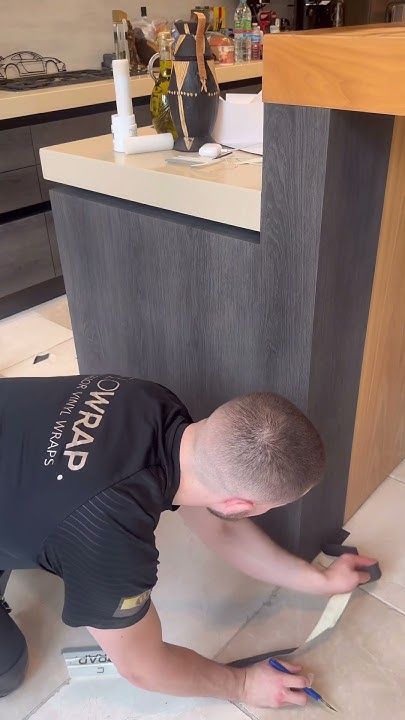 a man that is kneeling down on the ground next to a counter with scissors in his hand