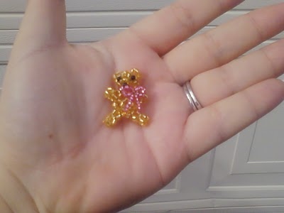 a hand holding a tiny gold teddy bear brooch