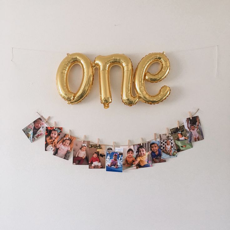 a gold balloon shaped like the number one hanging from a string with photos attached to it