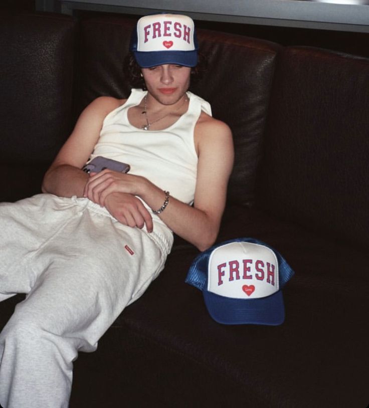 a man sitting on top of a couch next to a blue and white hat with the word fresh written on it