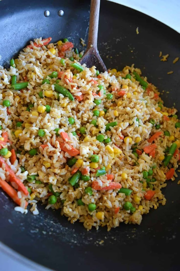 an egg fried brown rice with peas and carrots in a skillet on the stove