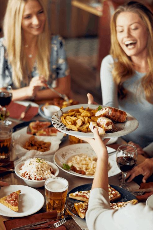 three women sitting at a table with plates of food and drinks in front of them