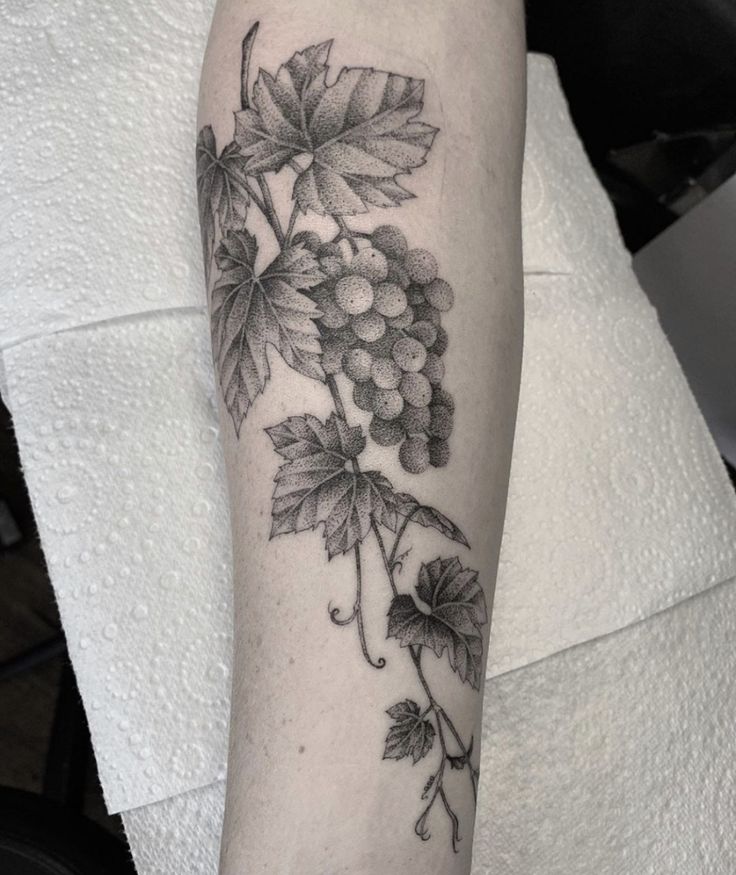 a black and white photo of grapes on the arm with leaves around it that are growing