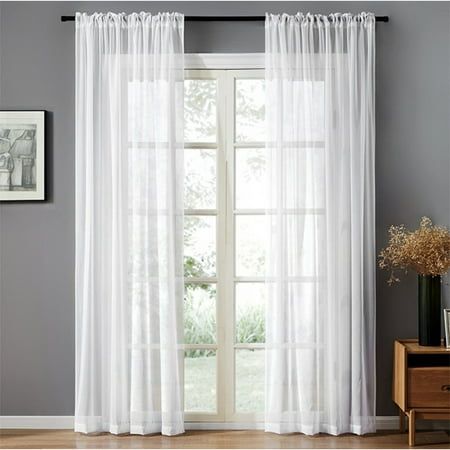 a white curtain hanging on the side of a window next to a wooden table with a vase