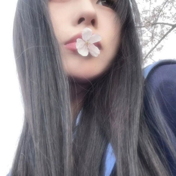 a woman with long gray hair and a flower in her mouth is posing for the camera