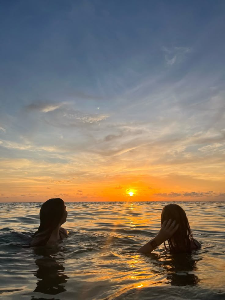 two people in the water at sunset with one holding her head up to her ear