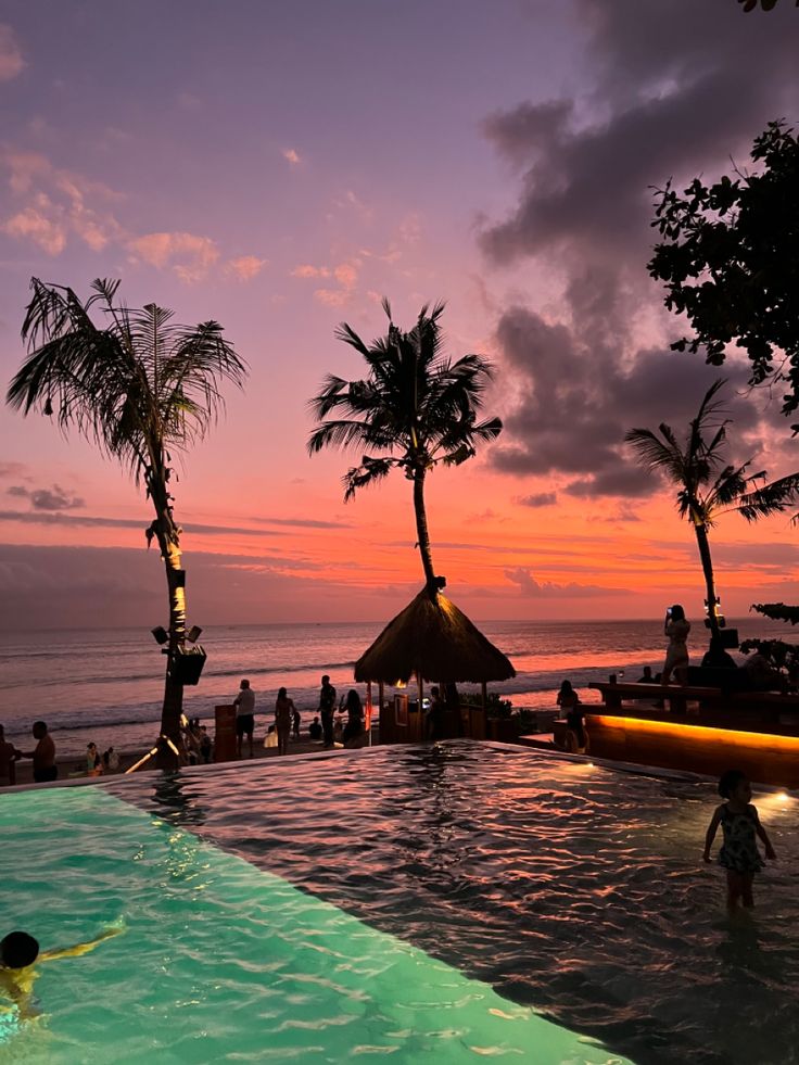 people are swimming in the pool at sunset