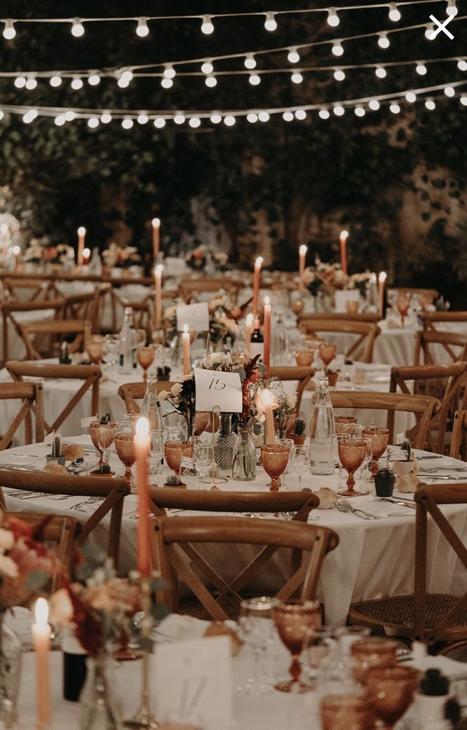 an outdoor wedding reception set up with white tablecloths, candles and centerpieces