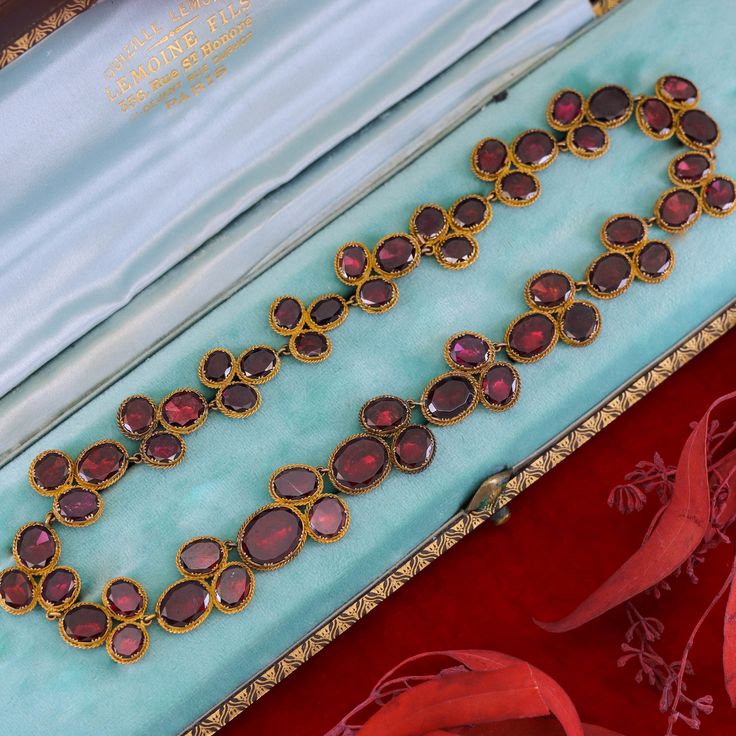 Experience the timeless elegance of this remarkable antique necklace dating back to the late Georgian era (circa 1820). Crafted with meticulous artistry, this exquisite piece showcases 54 oval flat-cut, foil backed garnets, set in 14k bloomed gold with closed backs, preserving their radiance for centuries. Measuring 16 inches in length, this antique necklace exudes a captivating charm and is in overall good condition. While there is one visible surface-reaching inclusion, it adds to the characte Luxury Oval Jewelry For Opera, Victorian Hallmarked Jewelry For Opera, Victorian Necklace With 17 Jewels In Oval Pendant, Antique Necklace With Historical Design For Formal Occasions, Antique Necklace With Historical Design For Formal Events, Victorian Necklace With Historical Design For Formal Occasions, Elegant Yellow Gold Garnet Necklace, Victorian Historical Design Necklace For Formal Occasions, Victorian Historical Design Necklaces For Formal Occasions