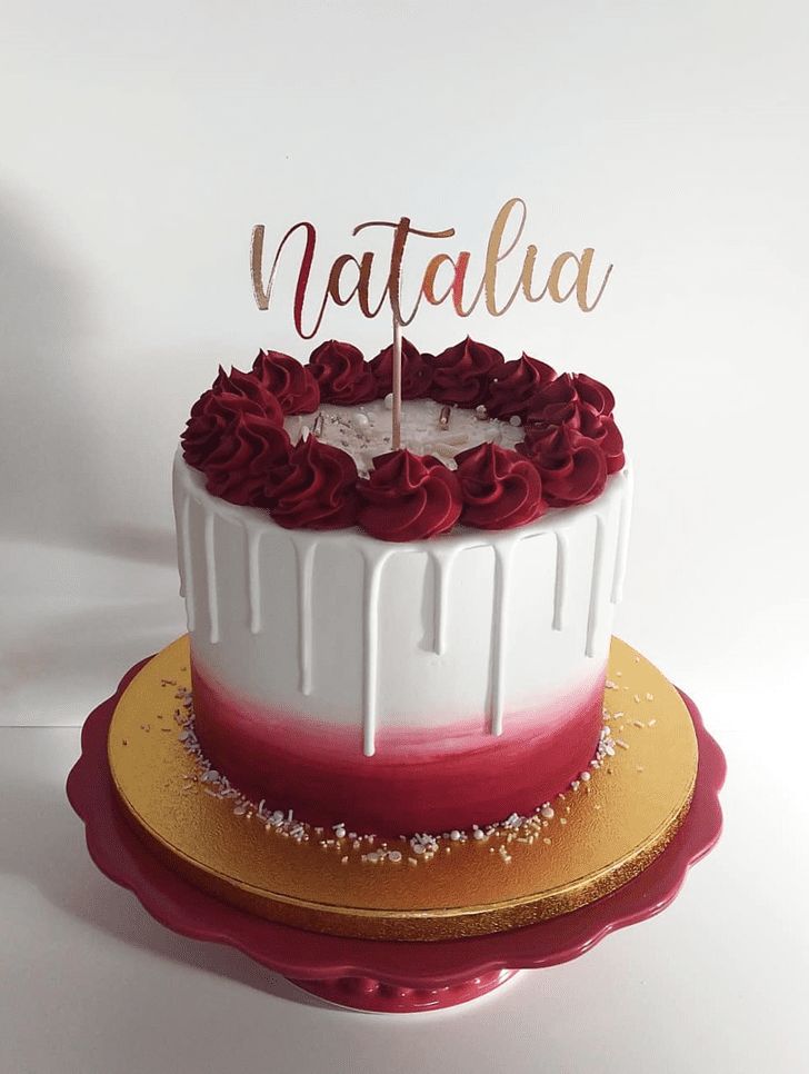 a white and red cake with the word nattalha on top, sitting on a gold plate