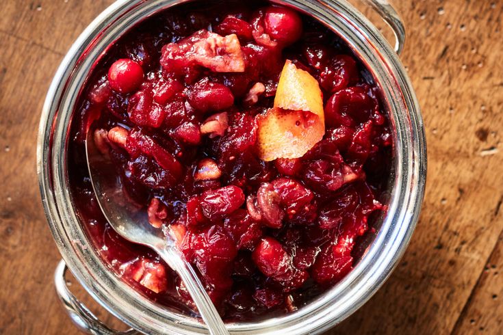 a glass jar filled with cranberry sauce on top of a wooden table next to a spoon