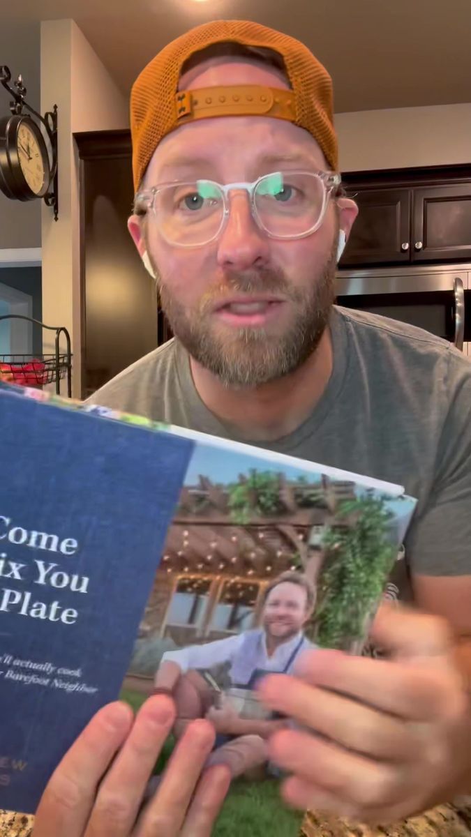 a man wearing glasses holding a cookbook in his hands and looking at the camera