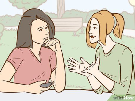 two women sitting at a table talking and one is holding her hand to her mouth