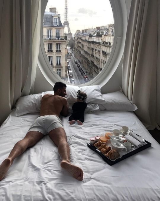 a man laying on top of a bed in front of a round window next to a tray of food