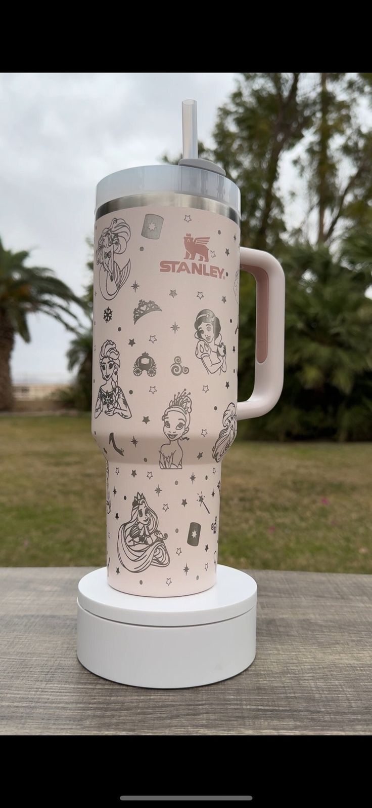 a travel mug sitting on top of a white stand in front of grass and trees