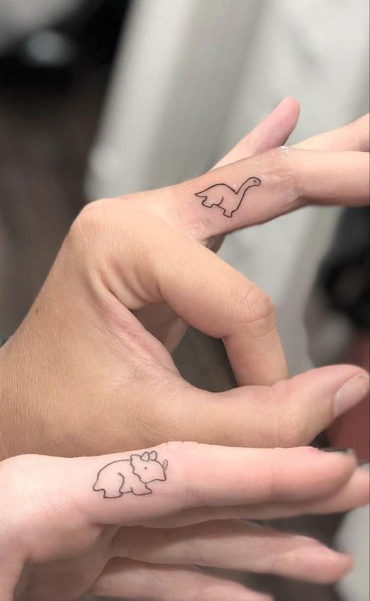 two people with matching tattoos on their fingers, one has an elephant and the other has a cat