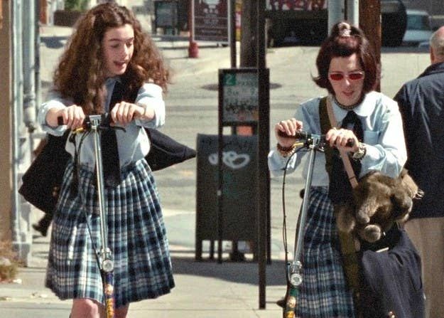 two girls are riding scooters down the street