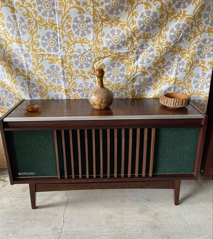 an old fashioned radio sitting on top of a wooden table next to a vase and bowl