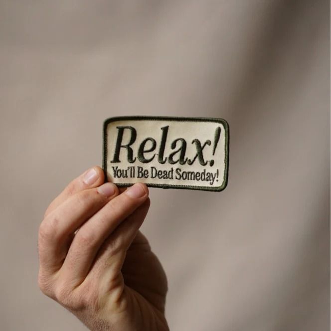 a person holding up a sticker that says relax you'll be dead somebody