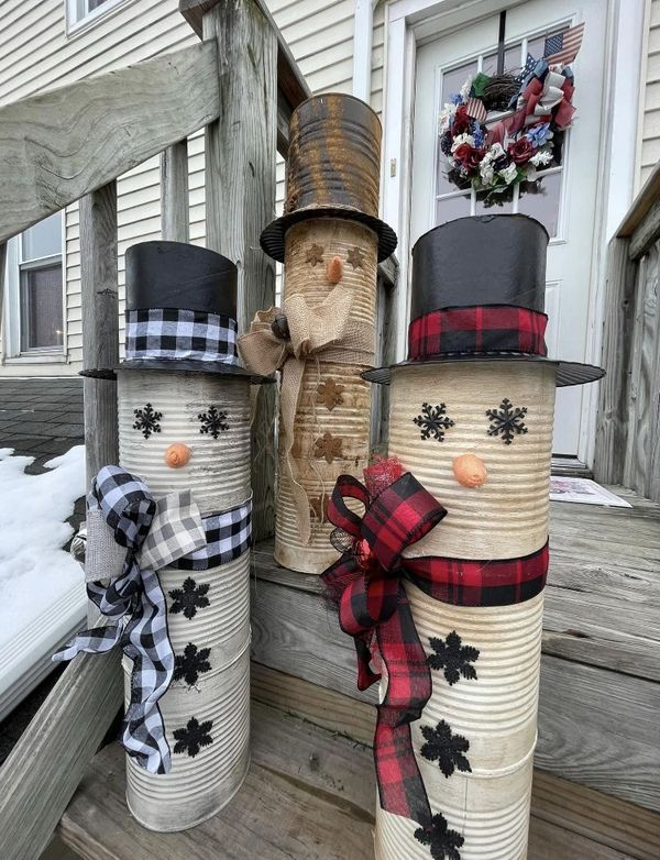 three snowmen made out of tin cans sitting on a wooden porch next to each other