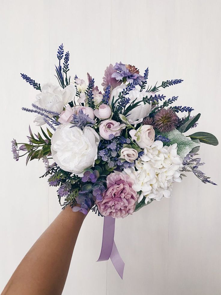 a bouquet of flowers is being held up by someone's hand with a purple ribbon