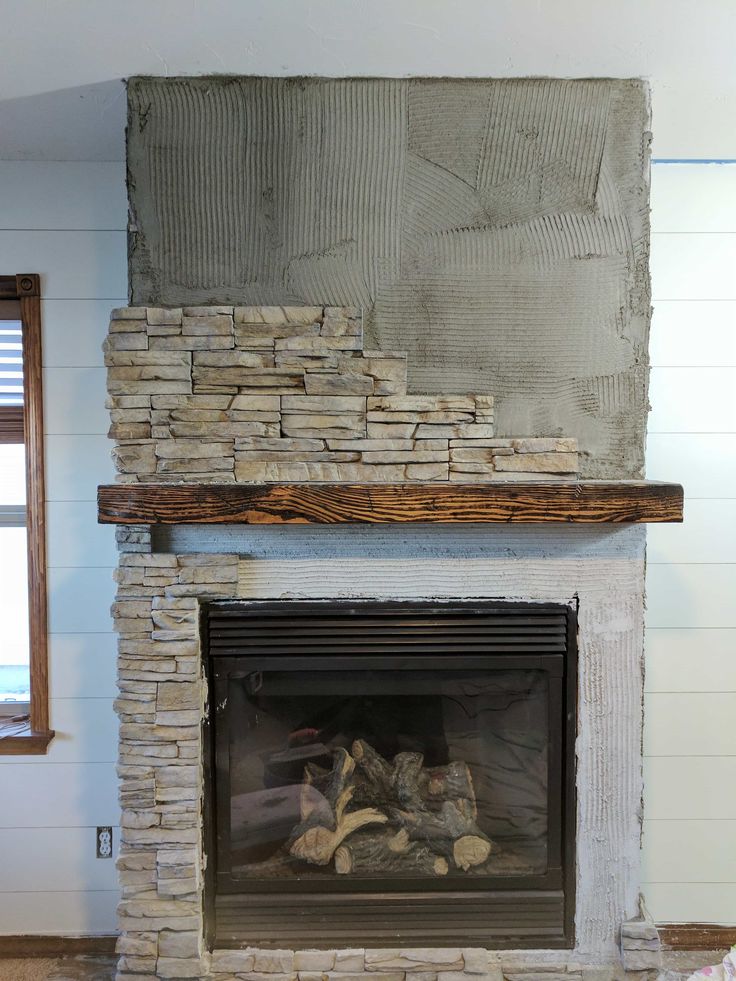 a fire place in a living room with a stone fireplace and wood mantel above it