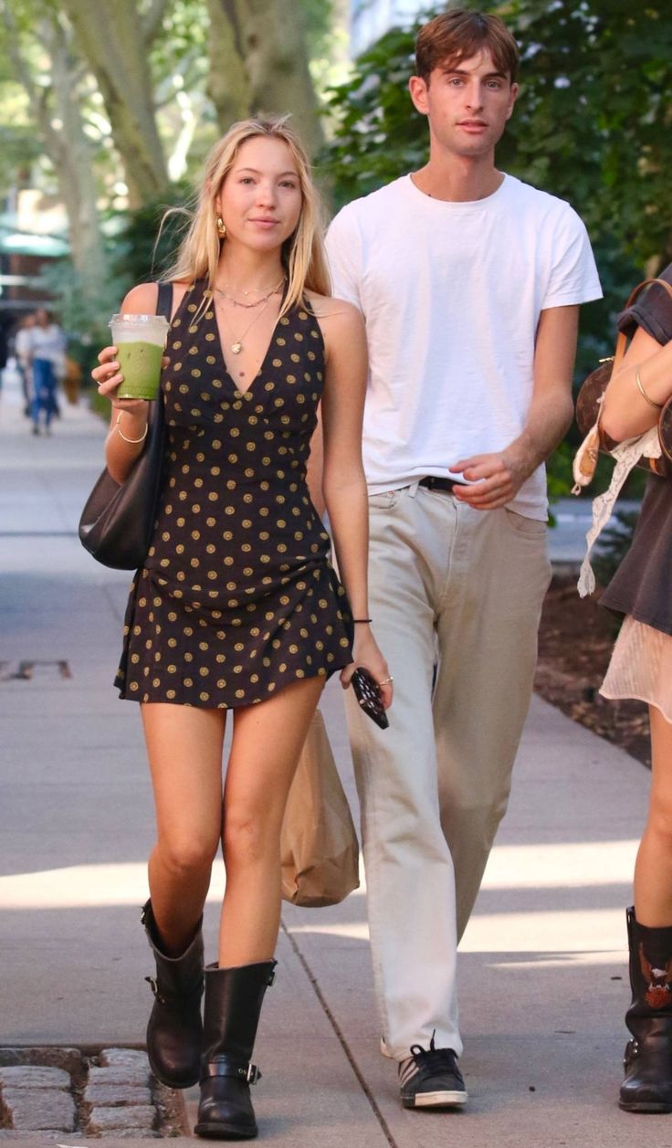 a man and woman walking down the street with drinks in their hands, one is holding a coffee cup