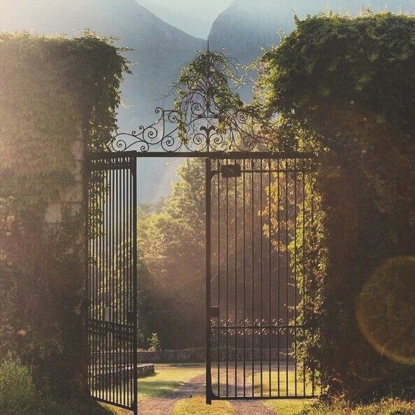 an iron gate is open to reveal a path through the garden with mountains in the background