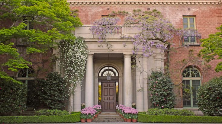 the front entrance to an old brick building with flowering trees and bushes on either side