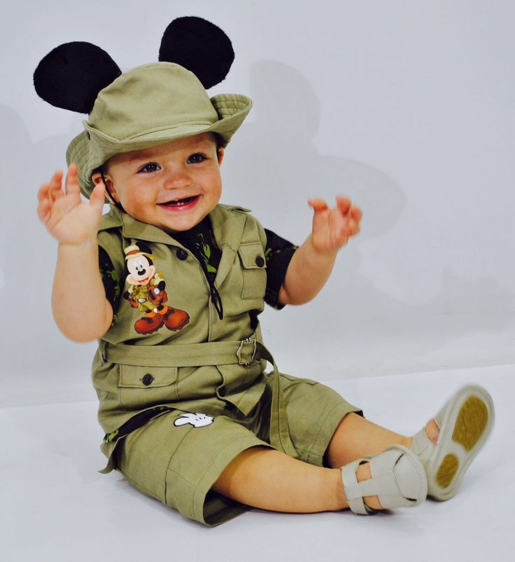 a little boy dressed up as mickey mouse sitting on the ground with his hands in the air