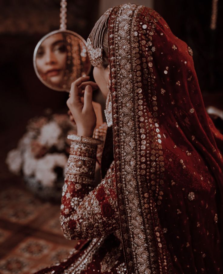 a woman is looking at herself in the mirror while wearing a red dress and veil