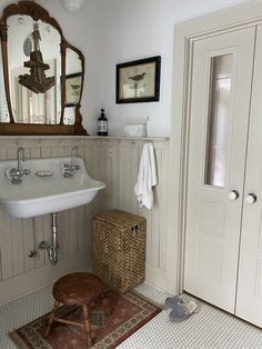 a white sink sitting under a bathroom mirror next to a wooden stool with a towel on it