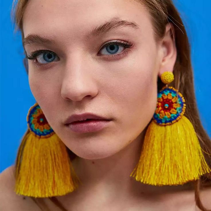 a woman with blue eyes wearing yellow tasseled earring and looking at the camera