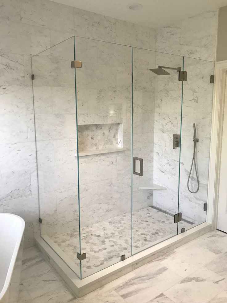 a bathroom with marble walls and flooring, including a walk in shower next to a white bathtub