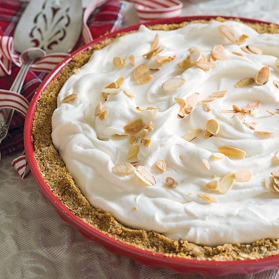 a pie with white frosting and almonds in a red dish on a table