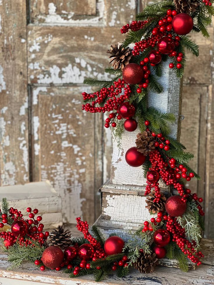 a christmas wreath with pine cones and red berries on it is sitting in front of an old door