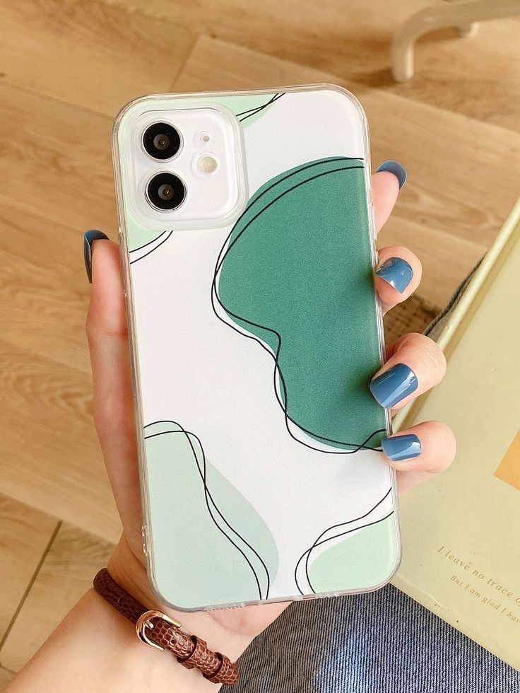 a woman holding an iphone case with a green and white design on the back, in front of a book